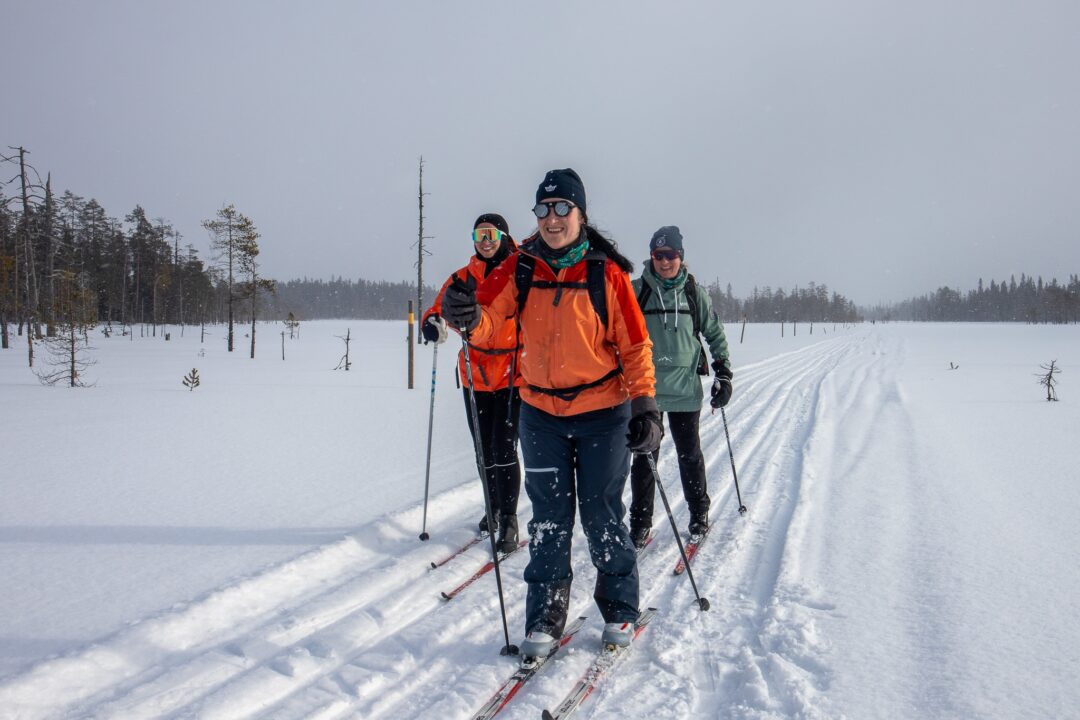 Women cross-country skiing on snowy Finland trail through a winter forest landscape