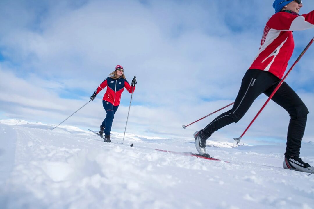 Women cross-country skiing in Norway on a snowy trail under a blue sky