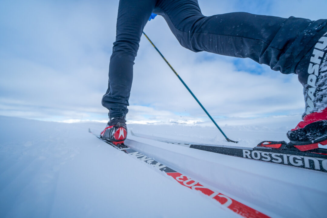 Woman cross-country skiing with poles on snowy track, skis marked “ROSSIGNOL” in misty landscape