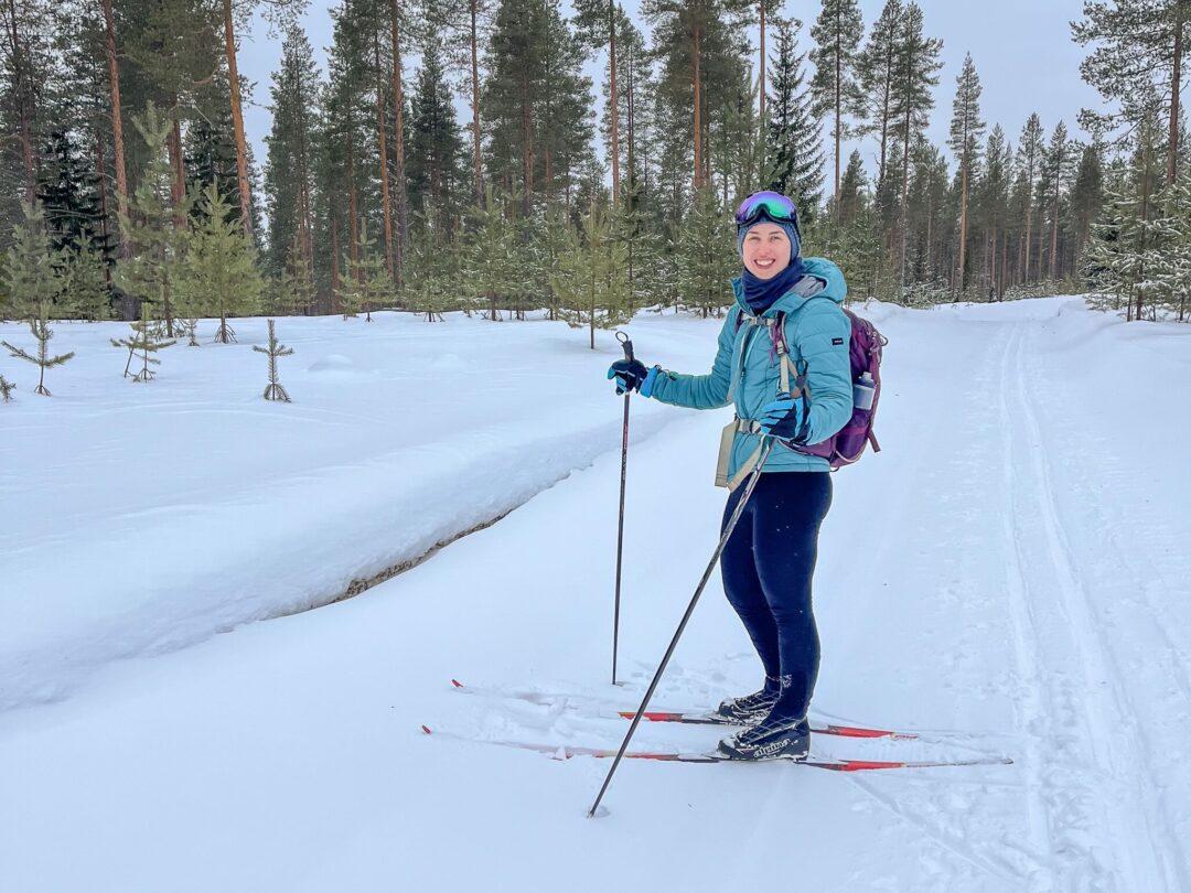 Woman cross-country skiing in snowy forest in Finland, holding skis on a groomed track