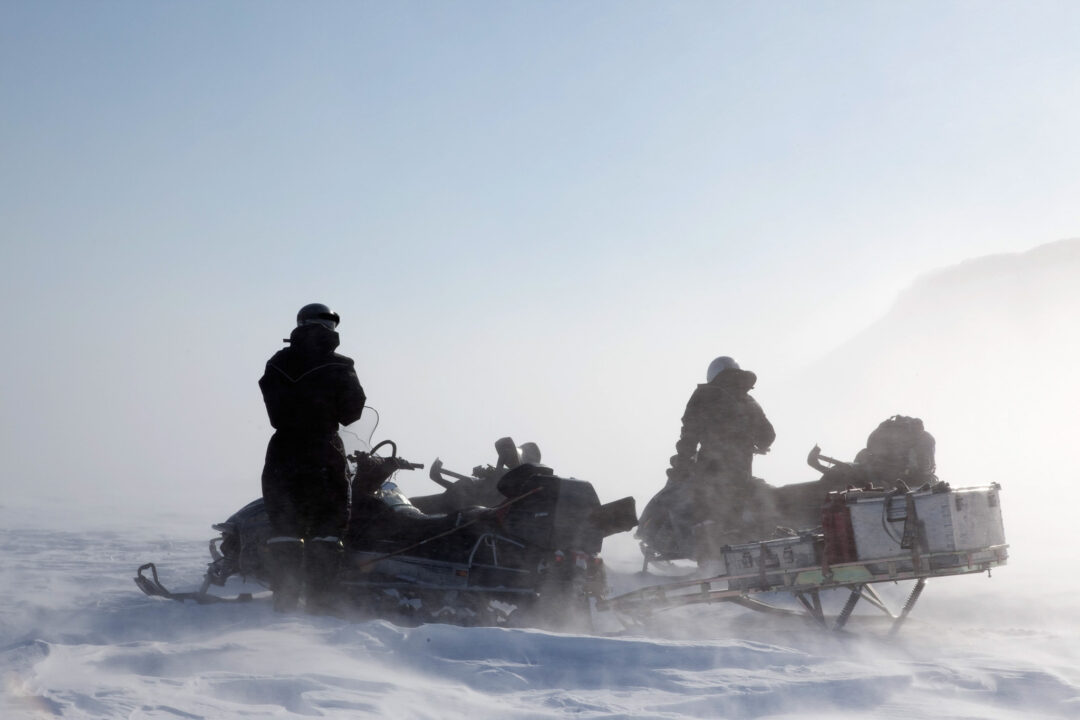 Snowmobile riders travelling across snowy terrain in heavy fog, with snowmobiles at the front
