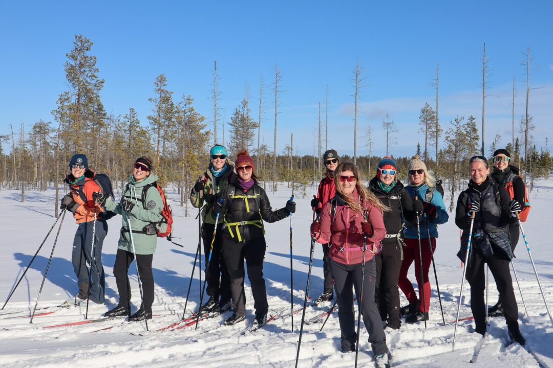 Women on a cross country ski tour in Finland, standing on snowy trail in a winter forest.