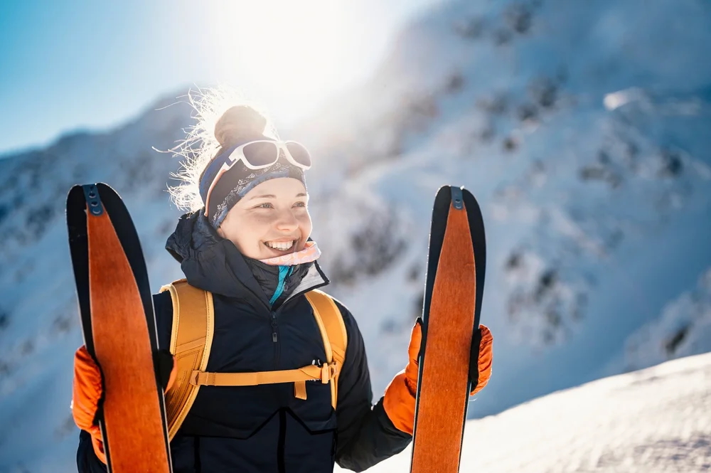 Smiling woman ski touring with skis on a snowy mountain slope in winter landscape