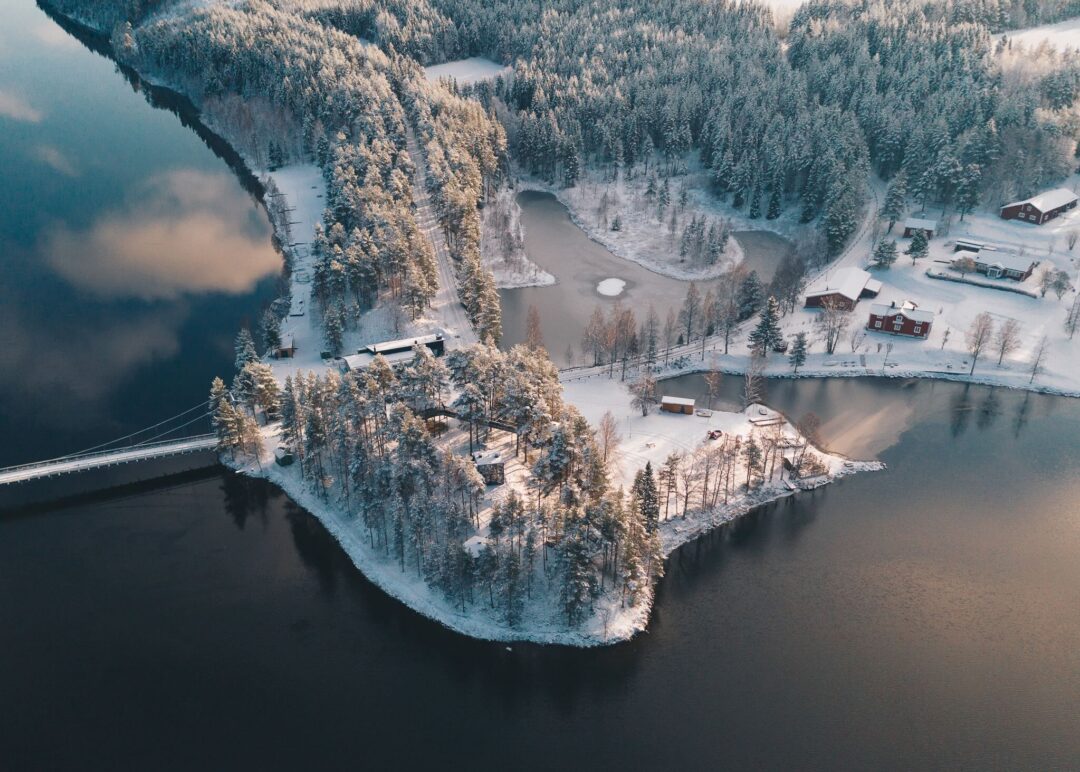 Aerial view of a snowy forest lakeside with winter cabins and frozen lake in Lapland