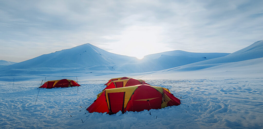 Red tents pitched on a snowy mountain landscape for wild camping and snow touring in winter
