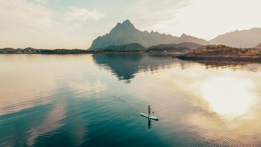 SUP paddleboarder on calm water in Lofoten with mountains at sunset