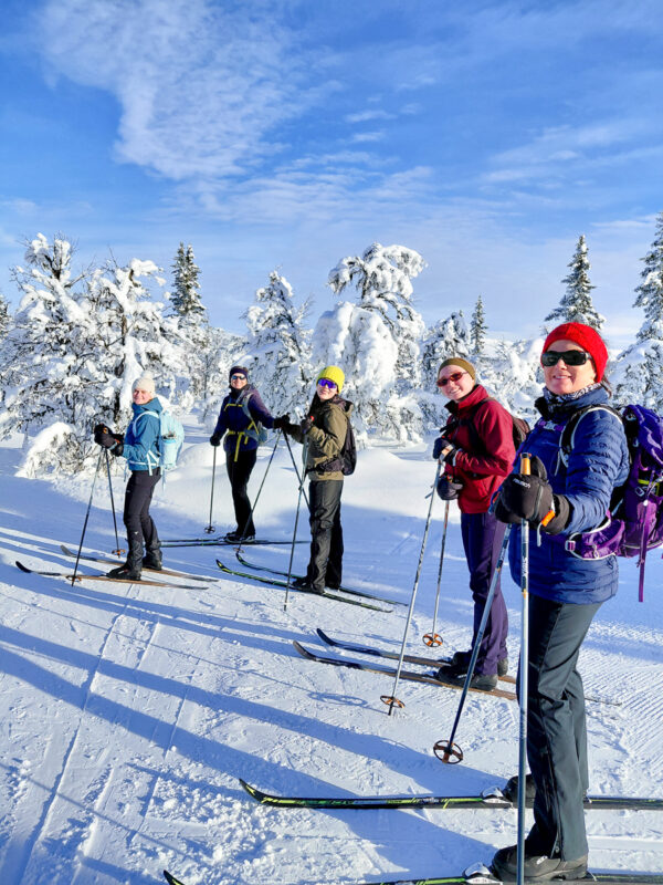 Women cross-country skiing on a snowy forest track, with skis and poles in winter daylight.