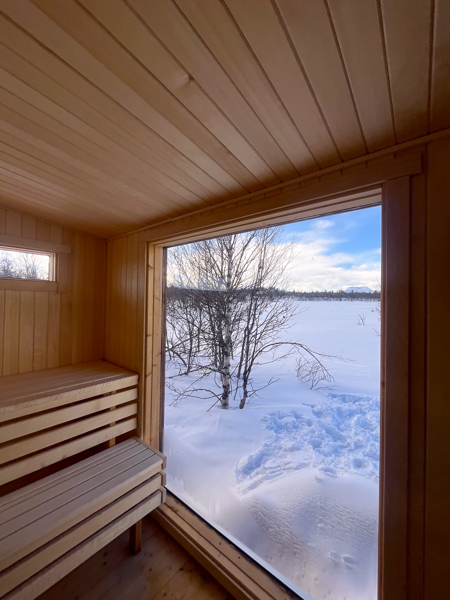 Wooden sauna with bench and window, showing a snowy winter landscape outside