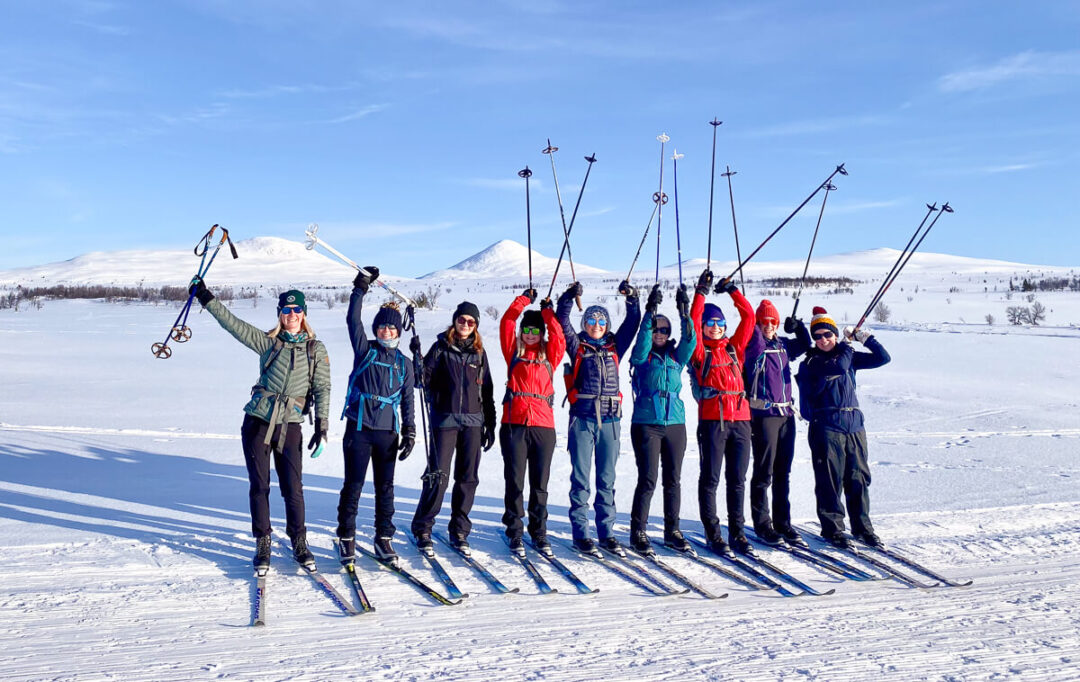 Women cross-country skiing group in snowy Norway landscape with mountains under blue sky