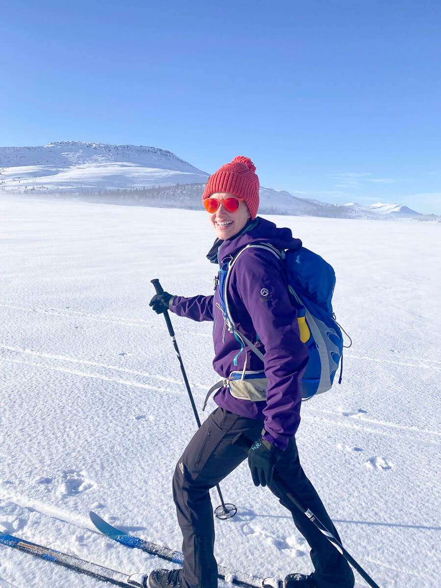 Women cross-country skiing in snowy Norway mountains, smiling with skis and poles.