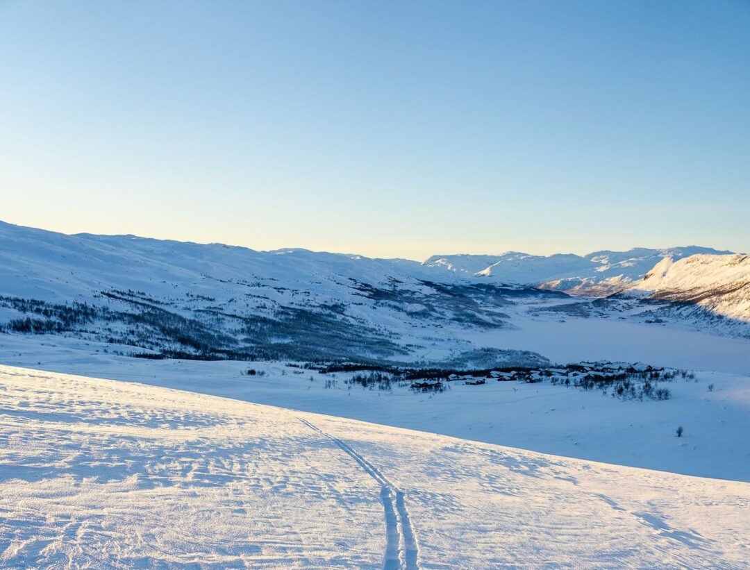 Snowy ski touring trail across Norwegian mountains at dusk with clear blue sky and winter landscape