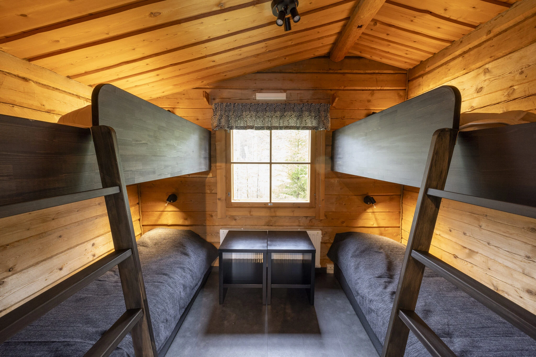 Wooden cabin interior with two beds and window light, featuring bench seating and warm timber walls