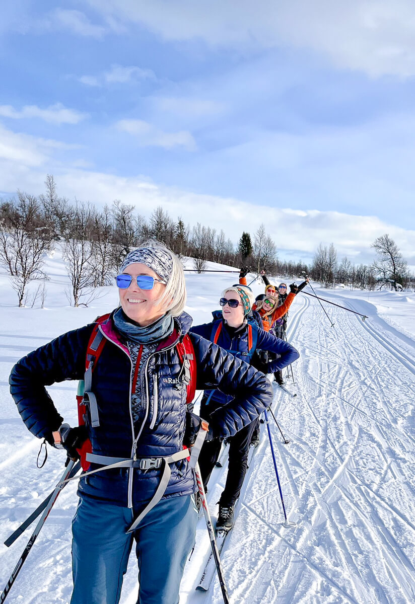 Women cross-country skiing in snowy Finland countryside on a sunny day, leaving fresh tracks