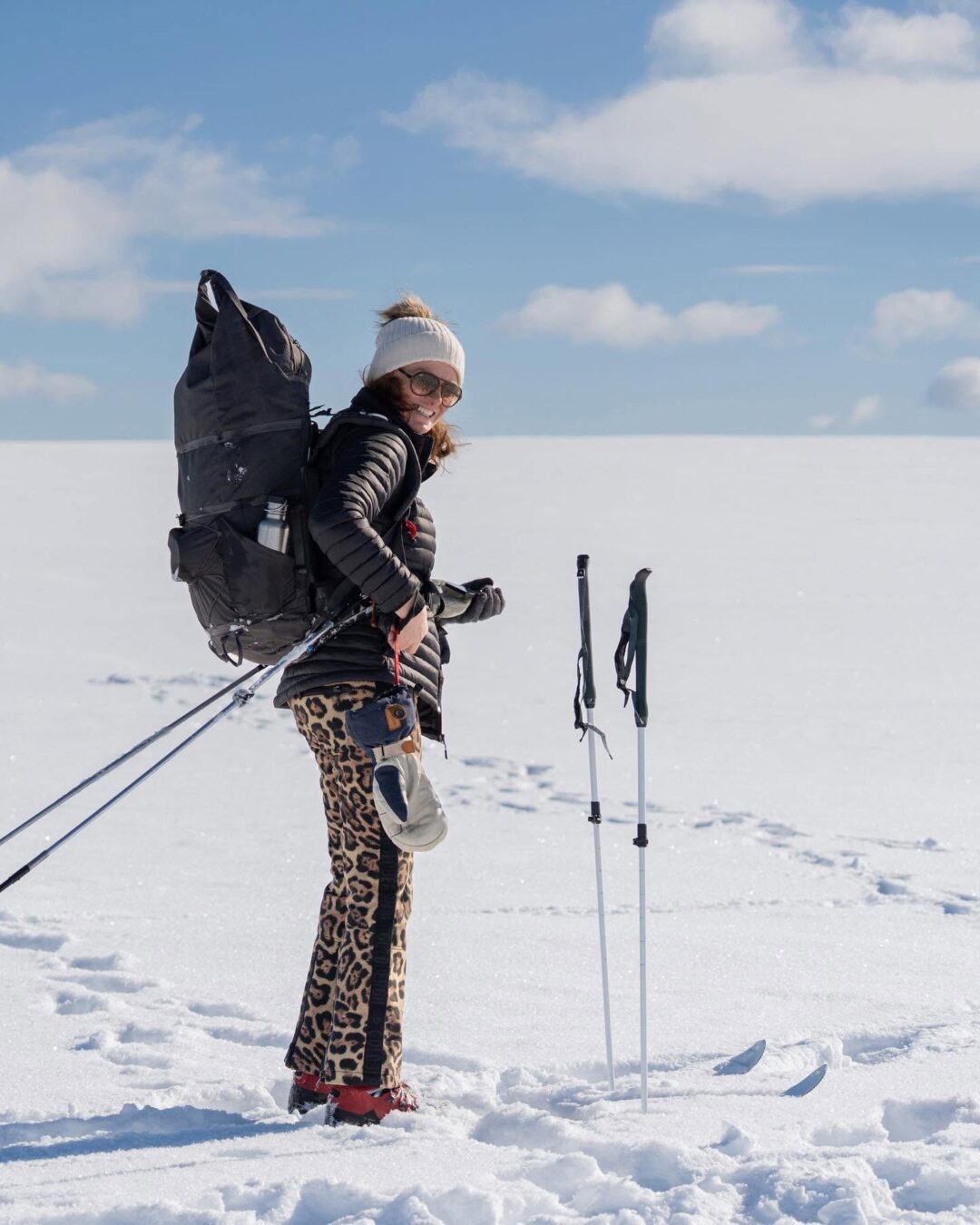 Woman backcountry skiing across snowy landscape, carrying a backpack and using ski poles
