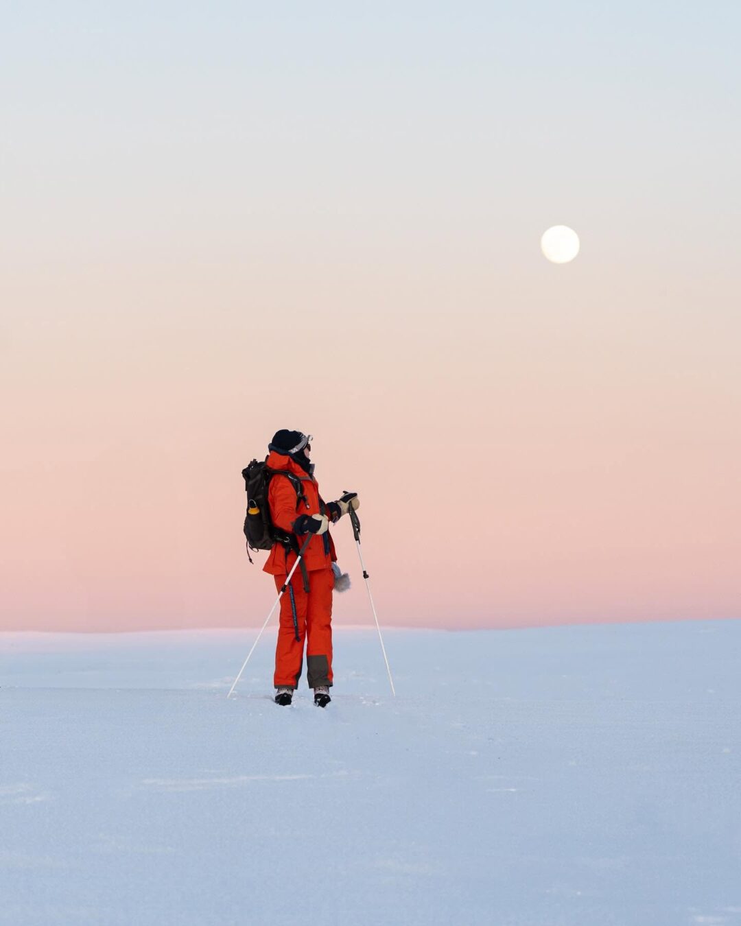 Woman in winter backcountry gear trekking across snowy landscape at dusk