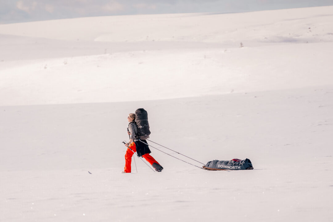 Woman pulling a sled on skis across snowy terrain during winter camping