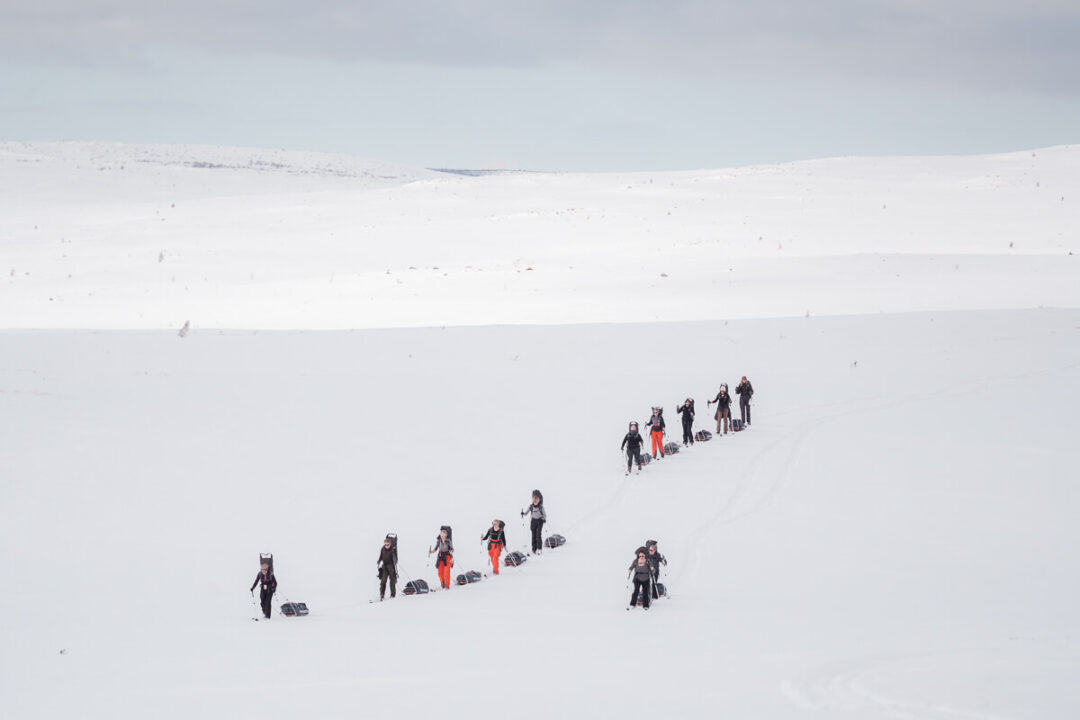 Women trekking with skis across a snowy backcountry slope in winter