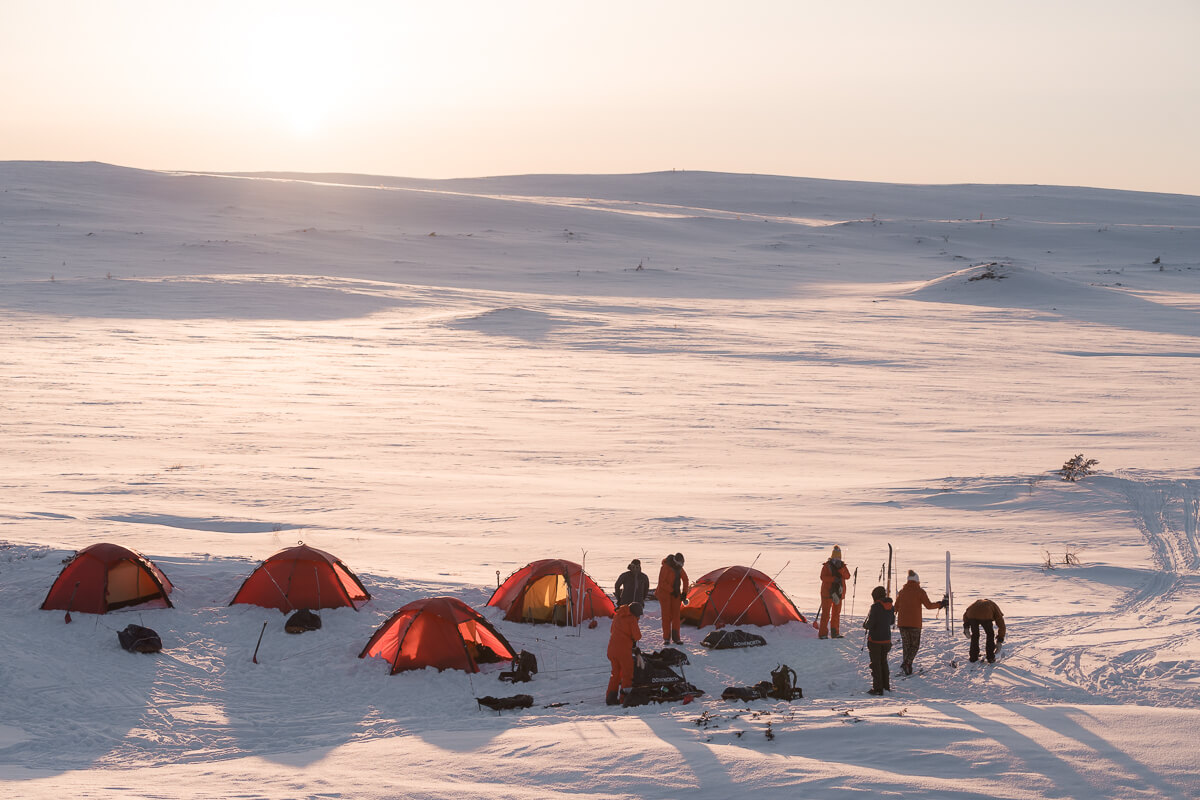 Women winter campers in Sweden with tents on snowy backcountry ski expedition at dawn