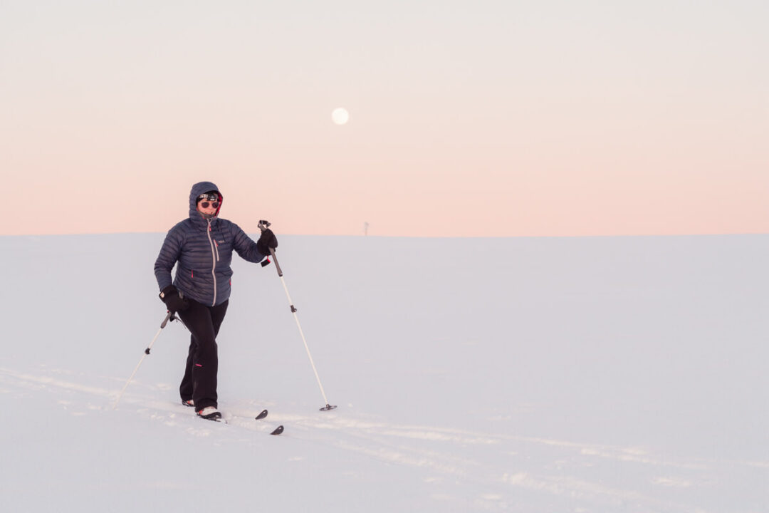 Woman cross-country skiing on snowy trail at dusk in a backcountry winter landscape