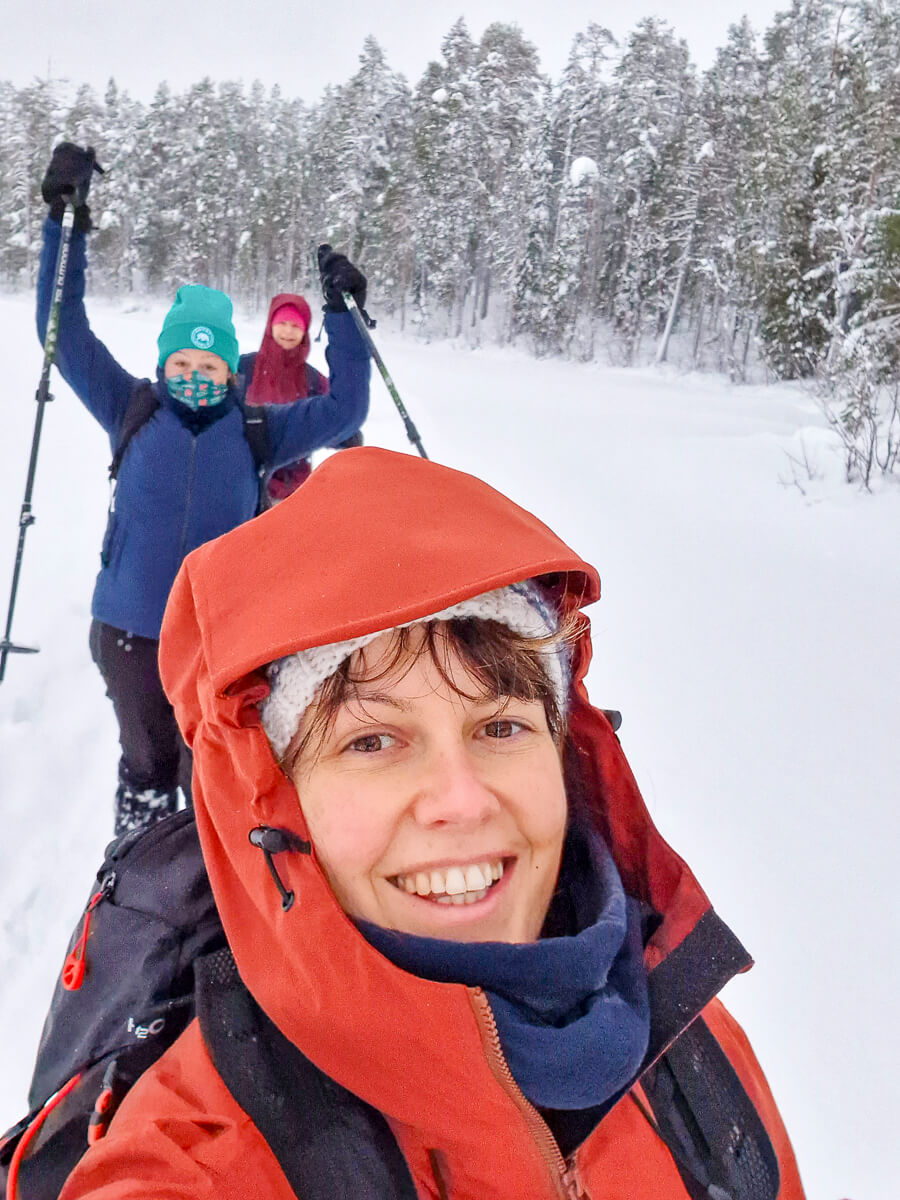 Women cross-country skiing in a snowy forest, bundled in winter hats, masks and red jackets.