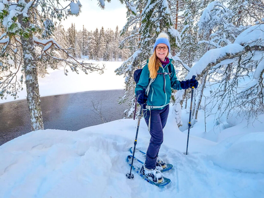 Woman cross-country skiing through a snowy forest beside a frozen river in winter.
