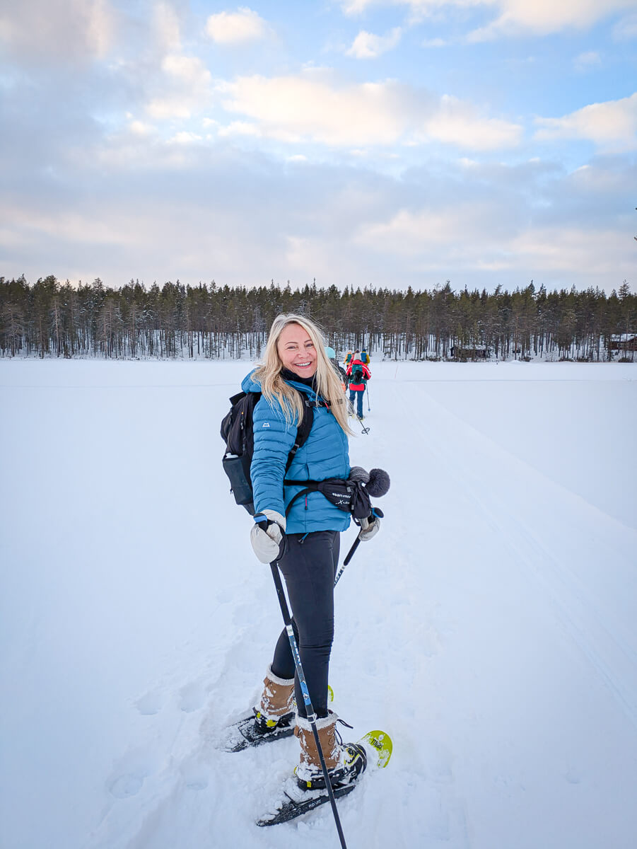 Woman snowshoeing across a snowy landscape with skis and winter gear in a forest clearing