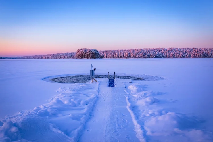 Snow-covered walkway leading to a small dock and platform on a frozen lake at dusk