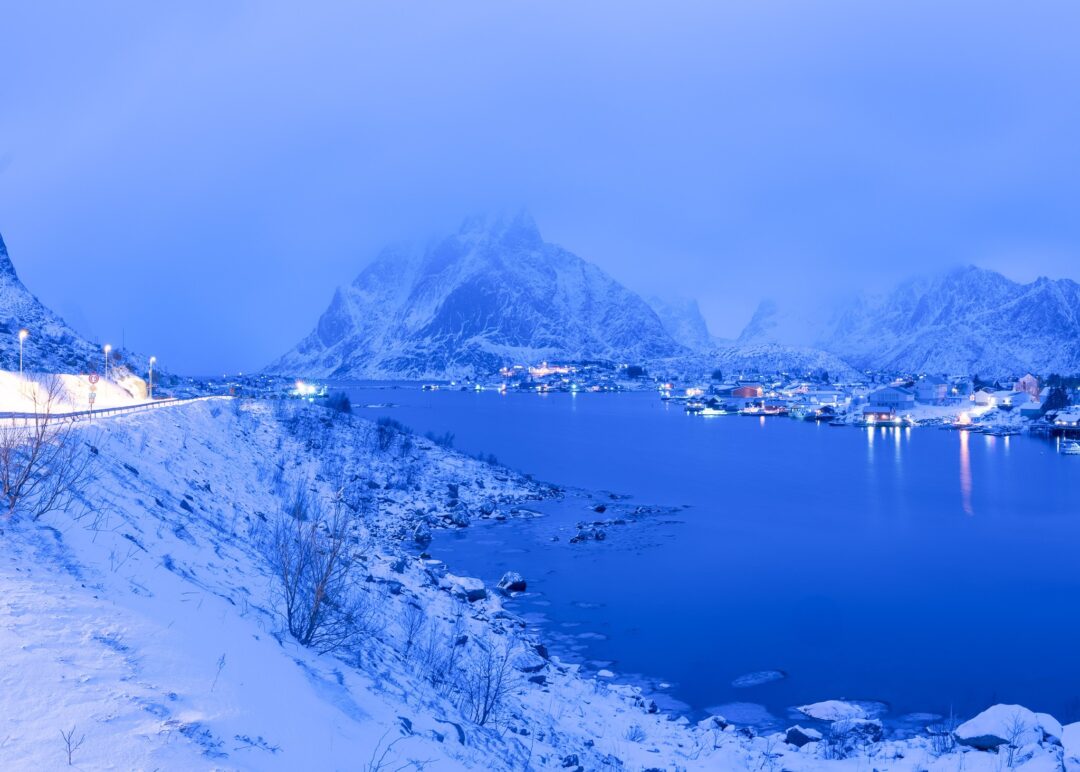 Snowy Arctic fjord landscape with mountain peaks and a winter harbour under blue twilight sky