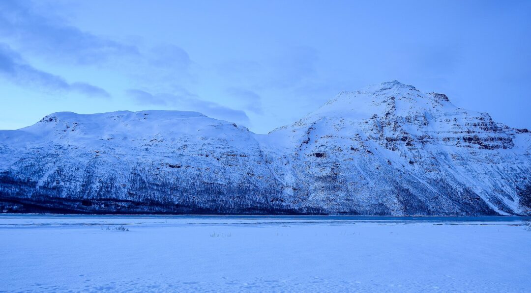 Snowy Arctic winter fjord with snow-covered mountains and blue polar night sky at dusk