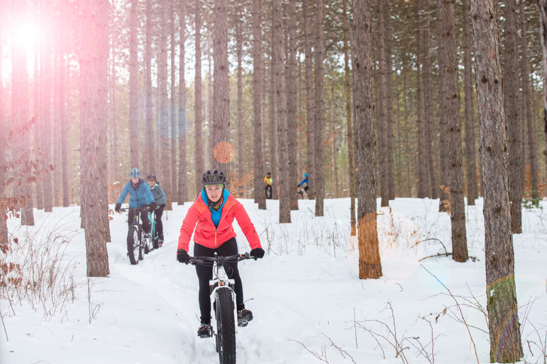 Women cycling on fat bikes through a snowy forest trail in winter