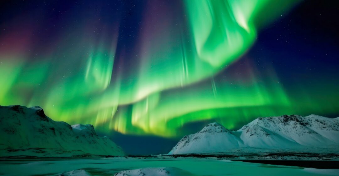 Northern Lights over snow-covered Arctic landscape at night, with dark mountains and sea ice in view
