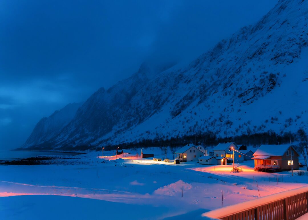 Arctic snowy village at night with northern lights and lit cabins