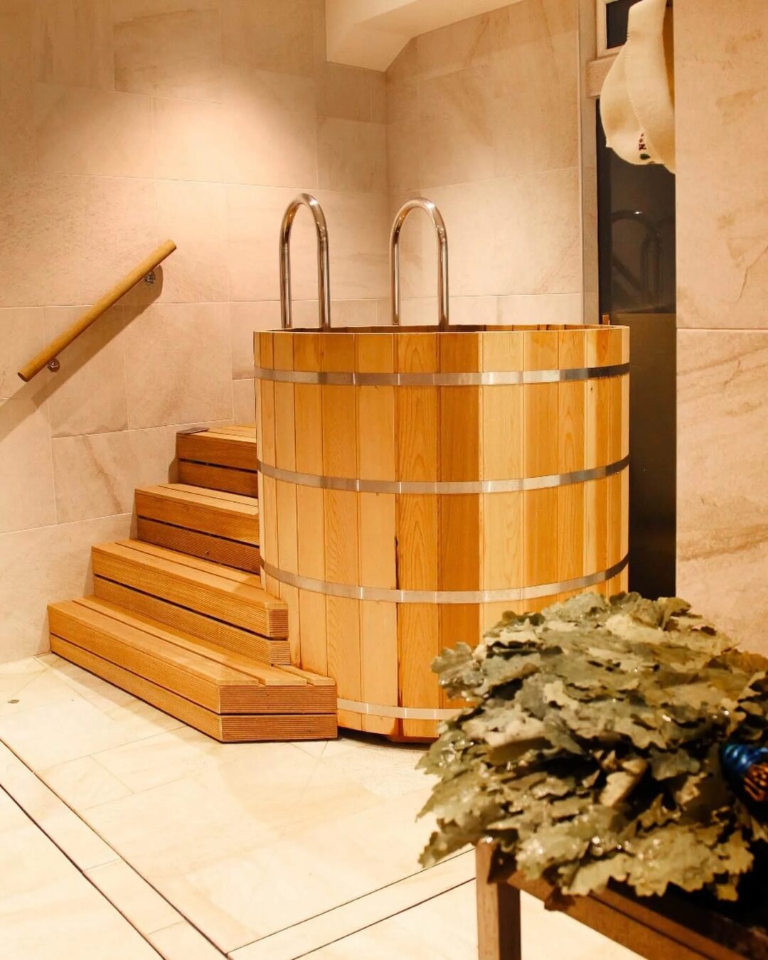 Indoor wooden sauna with barrel hot tub, steps, and stone bench in a steam room