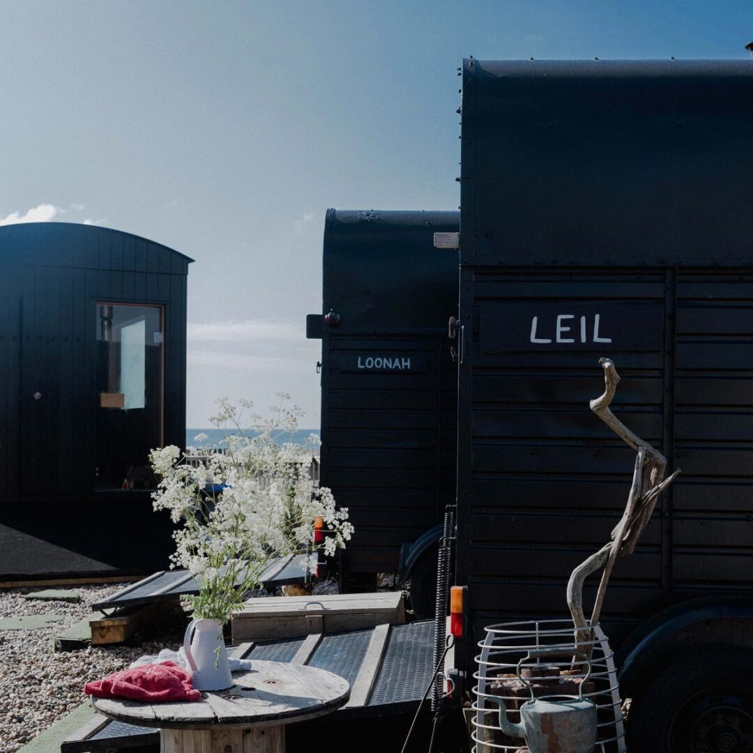 Portable sauna trailer with “LEIL” and “LOONAH” signs, outdoor deck with cold-dip barrel and flowers