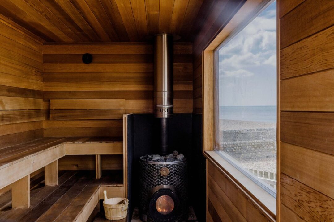 Sauna interior with wooden benches and stove, with a window showing a sea view