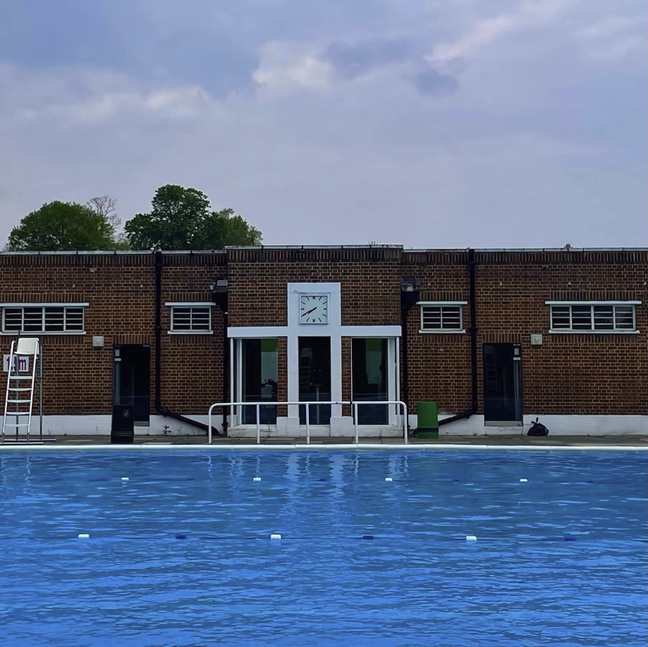 Outdoor swimming pool in front of a brick building with doors and windows, under a cloudy sky