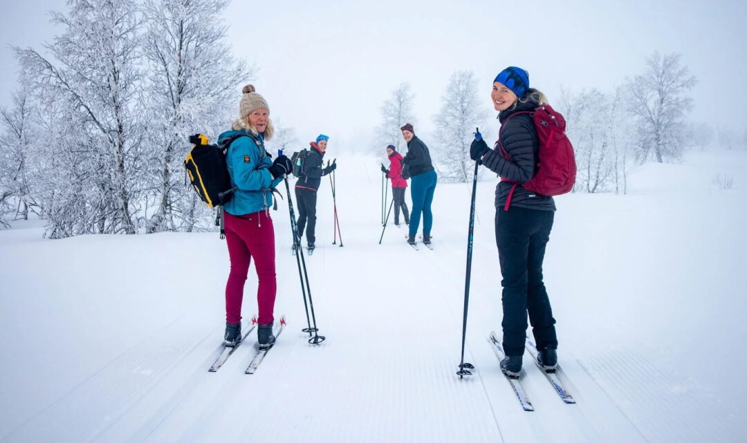 Women cross-country skiing on a snowy trail through a winter forest landscape