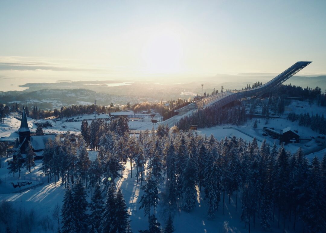 Snowy ski run through a winter forest at sunrise, overlooking a village with church spires