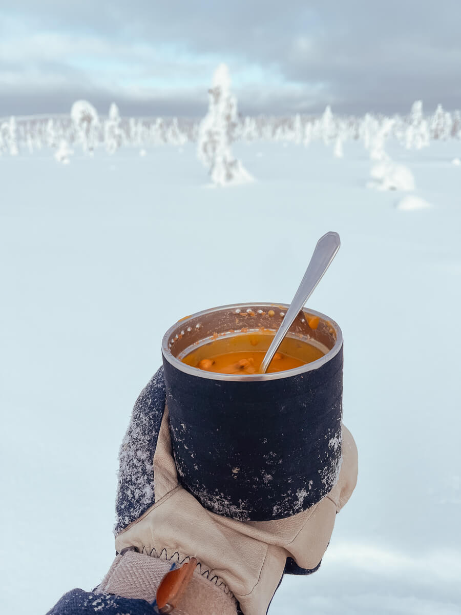 Woman holding a bowl of hot soup during backcountry winter camping in snowy landscape