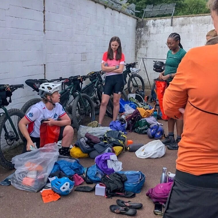 Women bikepacking group packing gear beside bicycles near a wall outdoors