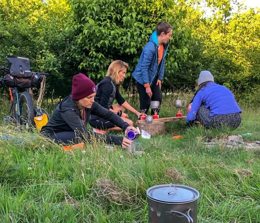 Women bikepacking camp cooking outdoors in a garden, preparing food at a small table