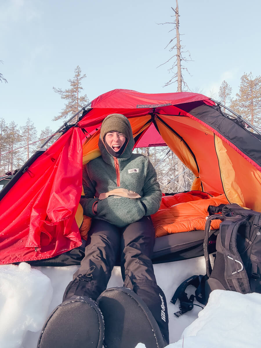 Woman inside a red and orange tent while winter camping in a snowy forest