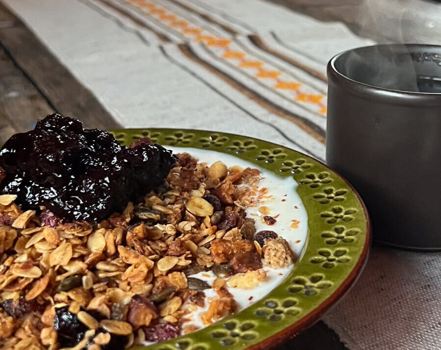 Plate of granola with berries and nuts, beside a metal mug for a camping breakfast