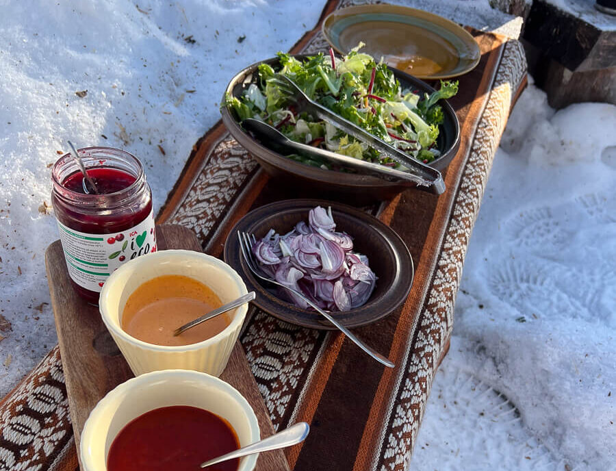 Winter camping food spread in snow: salad, onions, sauces and drinks on an outdoor table