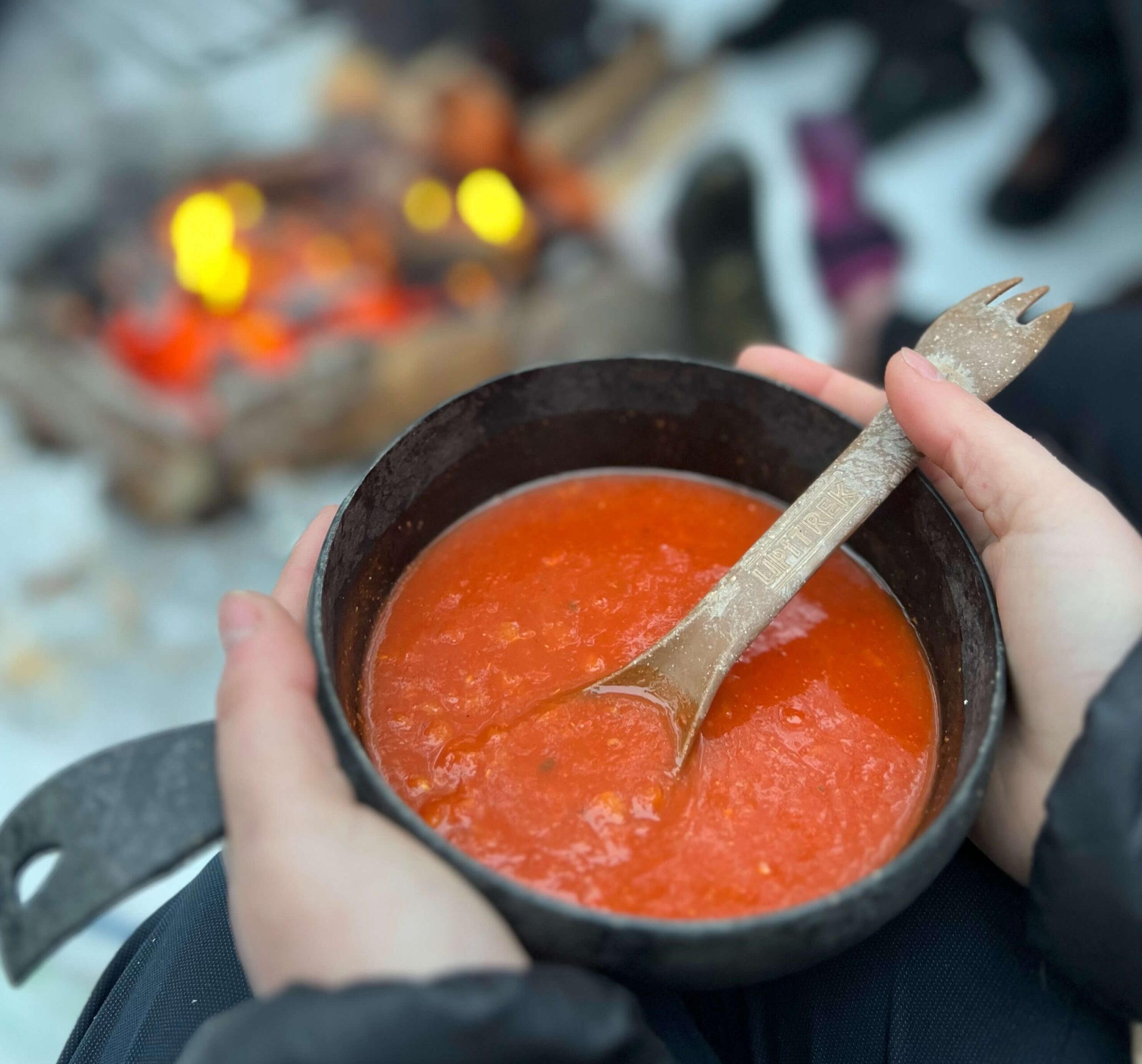 Hands holding a bowl of red soup outdoors in a snowy winter setting during a ski tour