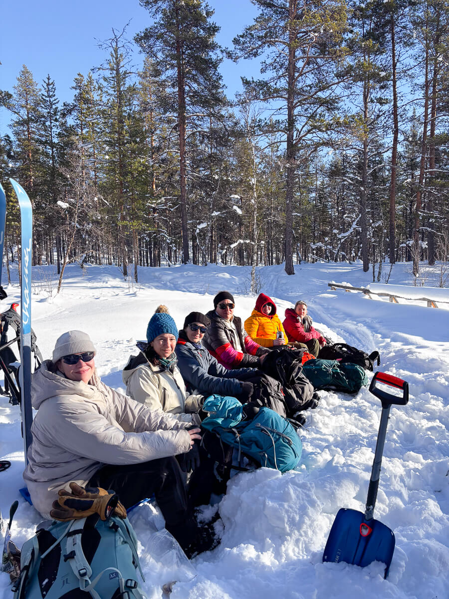 Women on a backcountry skiing break in snowy Lapland forest with pine trees and skis.