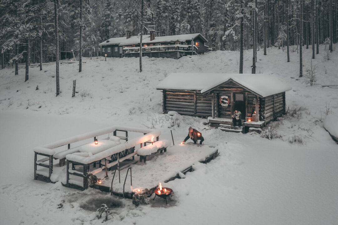 Winter camping with campfires beside log cabins in a snowy forest in Sweden