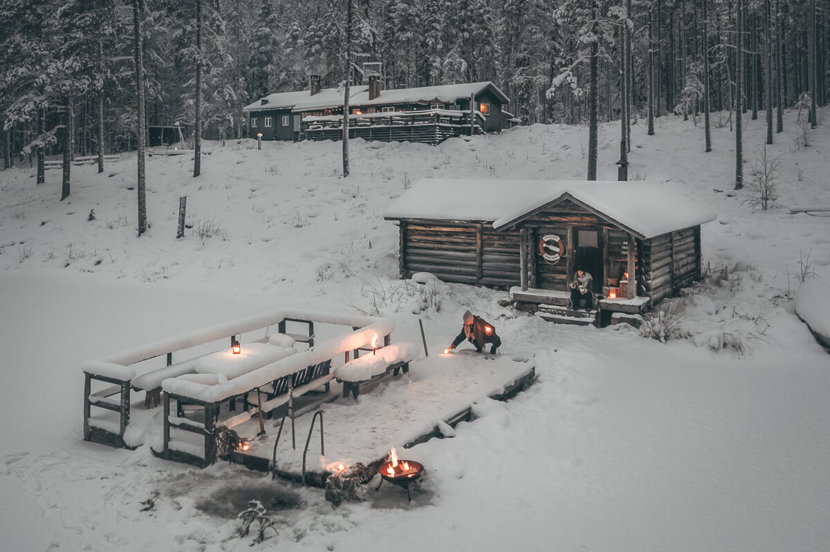 Winter camping with campfires beside log cabins in a snowy forest in Sweden