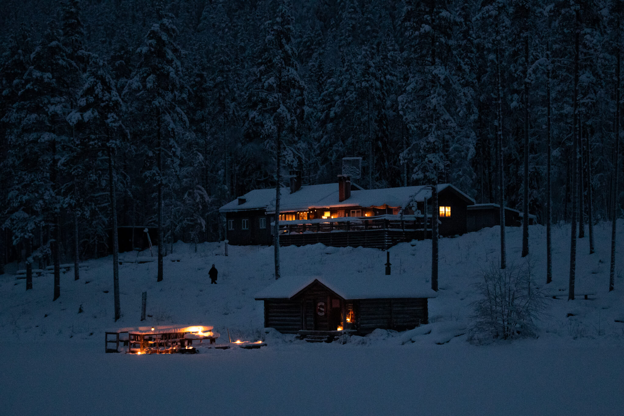 Lit cabins in a snowy forest at night, for winter camping expedition