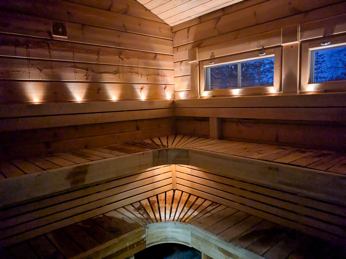 Wooden sauna interior with bench seating and windows, warm light and tiled floor